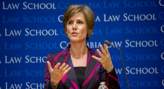 Sally Yates speaks wearing a black and magenta striped blazer. She stands in front of a Columba Law School backdrop.  There is a microphone and bottle of water on top of the podium. 